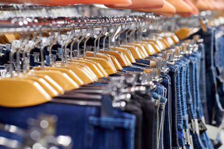 Row of hanged blue and black jeans on wooden hangers in shop. Many jeans hanging on rack. Row of pants denim jeans hanging in closet. Concept of buy, sell, shopping and jeans fashion.の写真素材
