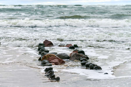 Scenic view of blue sea with foaming waves. Vintage long wooden breakwaters stretching far out to...