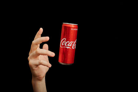 KALININGRAD, RUSSIA - MARCH 13, 2021 - Hand reaches to Coca Cola can, black background. Classic coke...