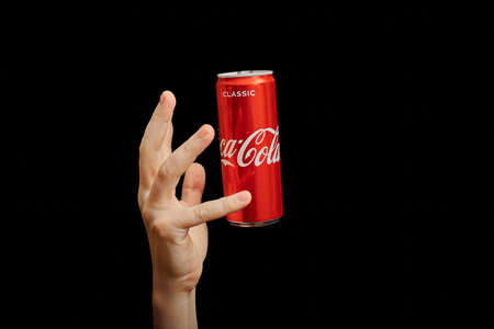 KALININGRAD, RUSSIA - MARCH 13, 2021 - Hand reaches to Coca Cola can, black background. Classic coke...