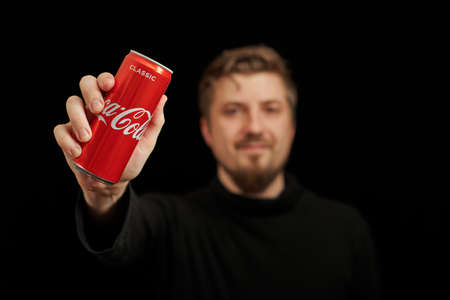 KALININGRAD, RUSSIA - MARCH 13, 2021 - Young guy with Coca Cola can in hand, black background....