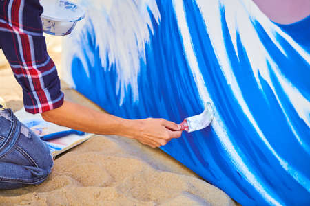 Female artist working on abstract acrylic painting, hand moving paint brush. Young woman creating modern masterpiece. Large canvas standing in open-air gallery, creative workshop outdoor close upの写真素材