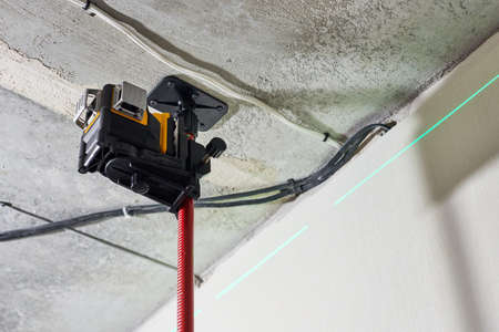 Laser level measuring tool with visible green laser beam on wall at construction site. Measuring...