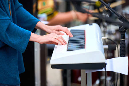 Musician woman playing on white synthesizer keyboard piano keys, focus on female hands on synthesizer. Musician playing musical instrument on stage, cropped image of person playing synthesizerの写真素材