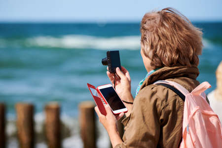 Brown-haired woman taking photos with digital camera, side view. Shooting video with digital camera,...
