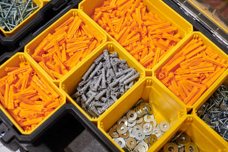 Many storage compartments filled with builders accessories containing screws, nuts, bolts, nails and other tools in workshop. Yellow case with small construction objects, close up photo for backgroundの写真素材