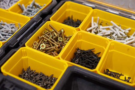 Yellow case with small construction objects. Many storage compartments filled with builders accessories containing screws, nuts, bolts, nails and other tools in workshop. Arranged neatly and organizedの写真素材
