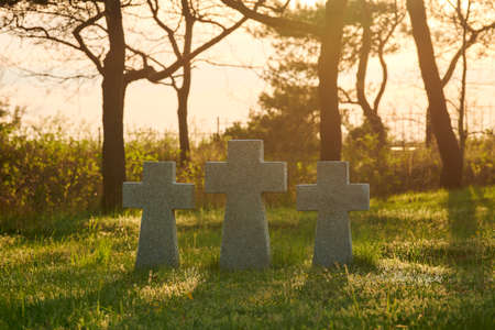Three catholic stone crosses on green grass at sunset in German military cemetery in Europe. Memorial for dead soldiers of World War II in Baltiysk, Kaliningrad oblast, Russiaの写真素材