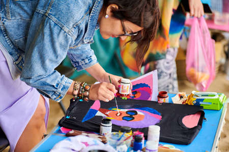 Svetlogorsk, Russia - 08.14.2021 - Female artist painting on black T-shirt using brush and fabric...