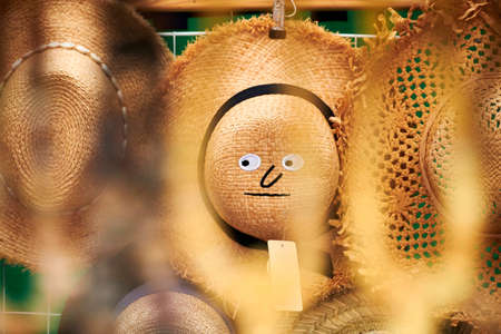 Street shop selling straw sun hats, funny face on summer floppy hat for tourists, disheveled harvest hat brim, beach style design. Sun protection headdress, touristic shopping and souvenirsの写真素材