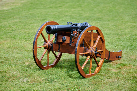 Restored cannon model for castle defense, green lawn background. Artillery large-caliber gun, old...