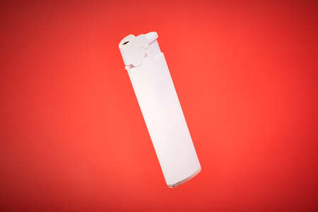 White pocket lighter on red background. Plastic lighter to ignite cigarettes, fireworks, candles or campfire. Disposable liquid gas igniter with piezo ignitionの写真素材