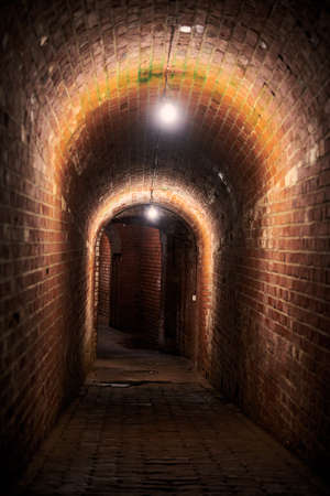 Brick tunnel in old German fort, red brick loft corridor with old wiring, industrial basement of...