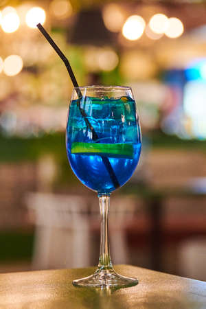 Blue Lagoon cocktail in glass with straw, night cafe light bokeh background. Tasty blue cocktail drink on cafe table. Blue liqueur Curacao with flavored vodka and lemonadeの写真素材