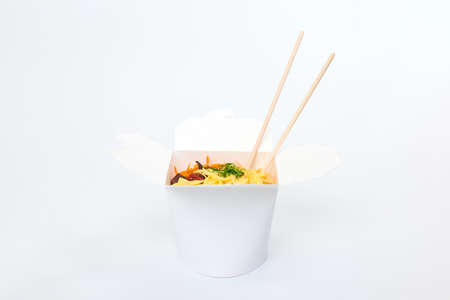 Rice wok with seafood and vegetables in white box and wooden chopsticks isolated on white background, close up. Open takeout box with wok and bamboo sticks. Asian food, fast food delivery conceptの写真素材