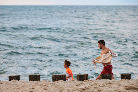 Svetlogorsk, Russia - 07.31.2021 - Father and little kid playing tag on sea beach, Baltic Sea background. Loving father and his son playing on beach. Funny family vacationのeditorial素材