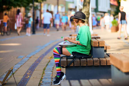 Zelenogradsk, Russia - 07.30.2021 - Street hank drum musician. Cute little girl playing tank drum on urban street. Young girl sitting on street bench and playing relaxing music on steel tongue drumのeditorial素材