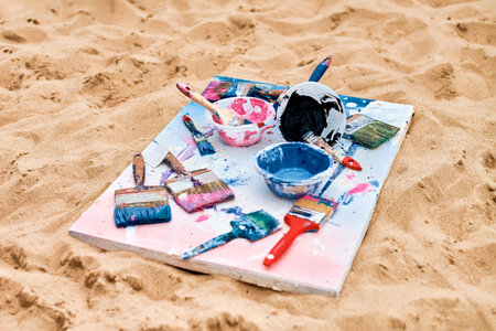 Two painted canvas in blue and pink colors with palettes of paints lying on sandy beach, artist's...