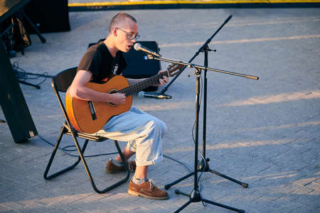 Svetlogorsk, Russia - 08.15.2021 - Young guy playing acoustic guitar and singing song in microphone,...