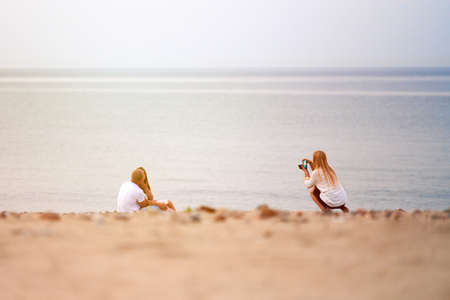 Couple in love backstage of outdoor photo shoot, professional female photographer shooting of loving couple on beach, sea background. Wedding love story photo shoot, beautiful seascape horizonの写真素材