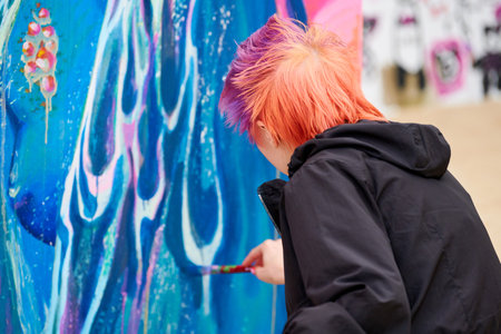 Woman painter with short multicolored hair painting beautiful colorful picture with paint brush,...