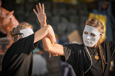 Two women in white theater mask dancing on art theatrical festival. Outdoor dance performance of two girls dancers in total black clothes style. Outdoor art theatrical performance festivalのeditorial素材