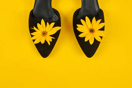 Suede black court shoes with yellow Jerusalem artichoke flower bud, yellow background. Leather...