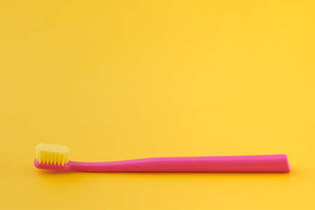 Pink toothbrush on yellow background for oral hygiene to clean teeth, gums and tongue. Manual plastic toothbrush for effective toothbrushing and healthy smile, isolated on yellow backgroundの写真素材