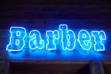 Blue neon wall sing with glowing barber inscription in loft barbershop interior. Retro LED neon text style on wooden wall on stylish barbershop reception, light strip design elementの写真素材