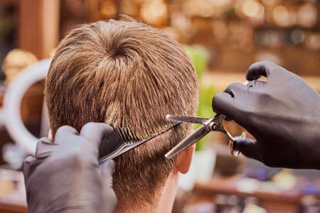 Male haircut in barbershop close up, client getting haircut by hairdresser with comb and scissors. Hairdresser makes hairdo in hairdresser salon, new stylish modern haircut for manの写真素材