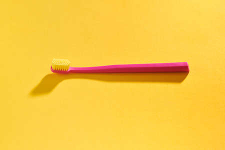 Pink toothbrush on yellow background for oral hygiene to clean teeth, gums and tongue. Manual plastic toothbrush for effective toothbrushing, hard light with shadow isolated on yellow backgroundの写真素材