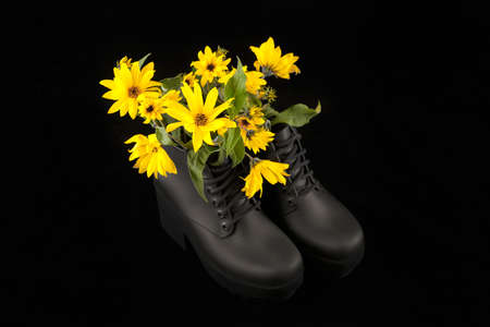 Black women platform boots with bouquet of yellow Jerusalem artichoke flowers, black background. Beautiful sunroot flowers in high heel platform boots with notched soles, shoe fragrance conceptの写真素材