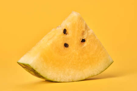 One piece of yellow watermelon with seeds on yellow background, delicious refreshing fruit. Sweet tasty water melon sliced piece with yellow flesh, yummy summer fruit for stay hydratedの写真素材