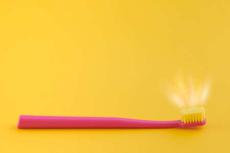 Pink toothbrush on yellow background for oral hygiene to clean teeth, gums and tongue. Manual plastic toothbrush with fresh shine near bristle isolated on yellow backgroundの写真素材
