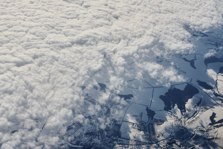 Aerial view over clouds top to snow covered rivers, fields and roads, winter fresh frosty air. Beautiful hazed sky aerial view to Earth troposphere, snowy abstract background textureの写真素材