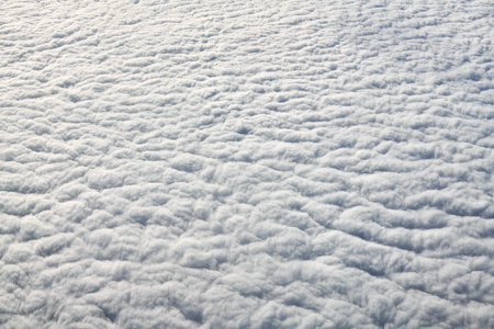 Breathtaking over clouds view from aircraft window, thick white blue clouds looks like soft foam, overcast with fresh frosty air. Beautiful cloudy sky view to troposphere, heavy cloudinessの写真素材