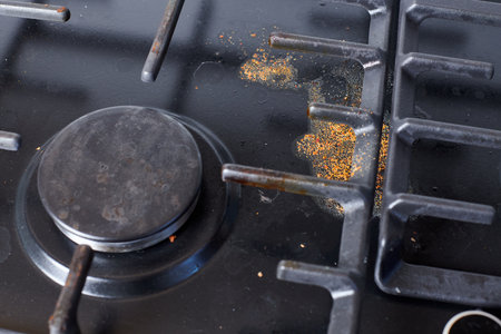 Unclean dirty kitchen black stove after soup boil over, dried food spots, fat stains dry food leftovers. Black stainless cooktop with gas burner stained in remains of fat food and oil splattersの写真素材