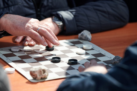 Outdoor drafts competition on paper checkerboard on table, close up players hands. Outdoor checkers board game between two amateur players at sunny day, development of strategic thinkingの写真素材