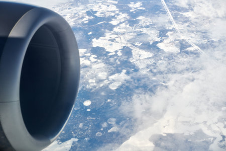 Aerial view from airplane window over clouds top to aircraft turbine and snow covered rivers, fields and roads, winter fresh frosty air. Beautiful hazed sky aerial view to Earth troposphereの写真素材