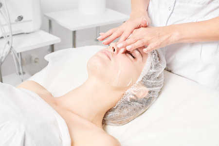 Beautician smoothes sheet mask on woman face for rehydrate face skin, procedure in beauty salonの写真素材