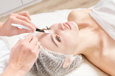 Beautician rubbing cream with brushes into woman face skin for rejuvenation, cosmetic procedure