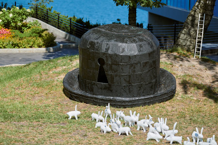 Art installation big black hat with keyhole on green grass and white artificial rabbits around lawnの写真素材