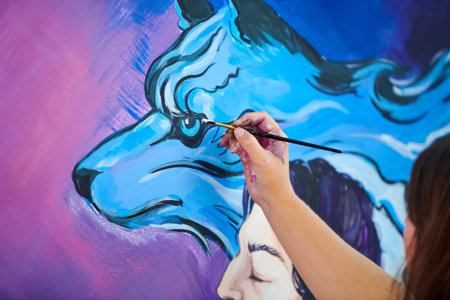 Woman artist hand holds paint brush and draws surreal fantasy image on canvasの写真素材