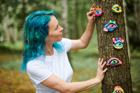Young woman with turquoise dyed hair in white T shirt considering handmade colorful eye amuletの写真素材