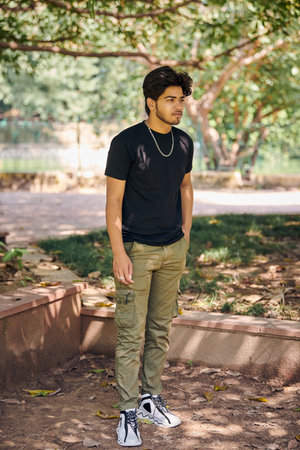 Attractive young indian man full height portrait in black t shirt, silver neck chain in green park