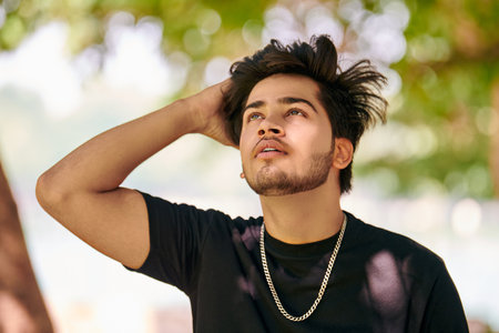 Attractive young indian man portrait in black t shirt and silver neck chain on green park backgroundの写真素材