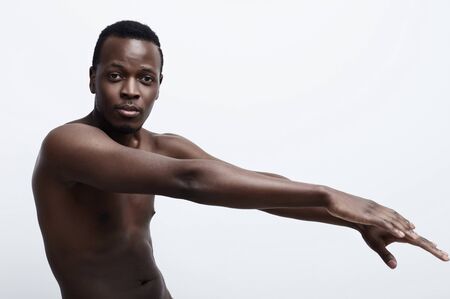 Close up studio shot of african american shirtless man with athletic body moving or dancing in front of grey wall posing at the camera.health and beauty conceptの写真素材
