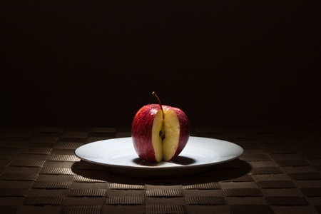 Red apple missing a slice on gold rimmed white plate in the spotlightの写真素材