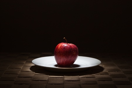 Organic red apple on gold rimmed white plate in the spotlightの写真素材