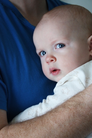 A baby with a brooding expression, being held by his father and snuggling into daddy s chestの写真素材